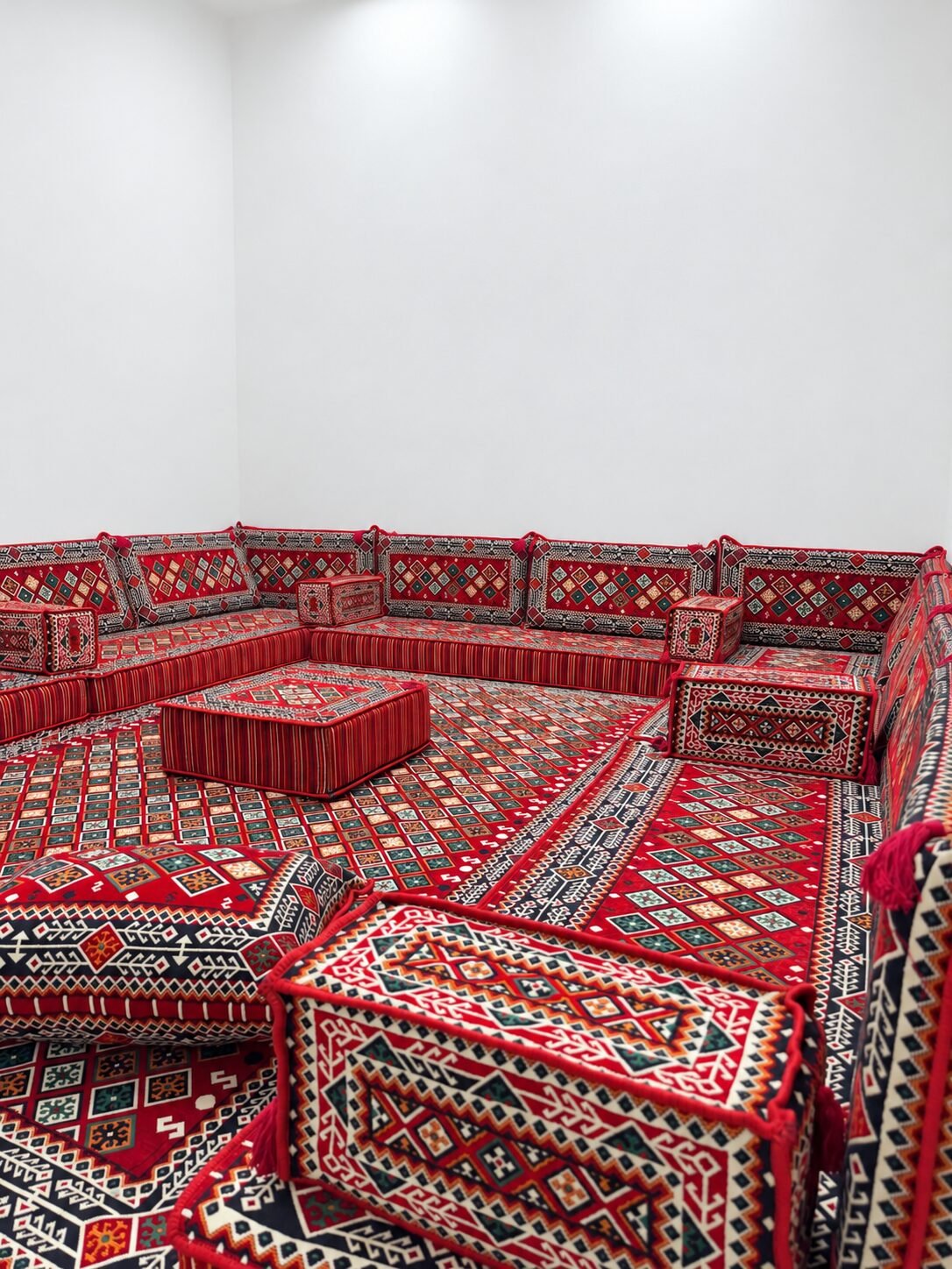Corner of the Anzaran red Sahrawi majlis with diamond-pattern back cushions, armrests and a striped pouf