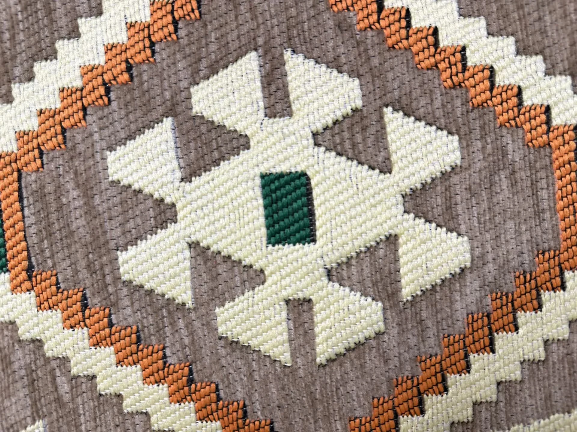 Macro view of the woven fabric: ivory, terracotta orange and green motifs on a beige ground