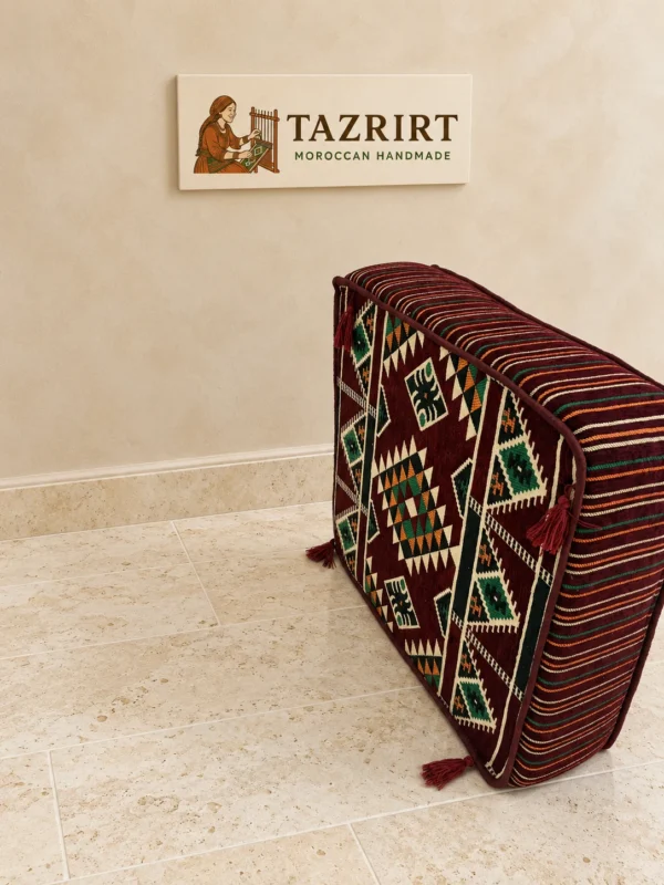 Burgundy kilim floor pouf standing upright, showing its patterned top, striped piped sides and corner tassels.