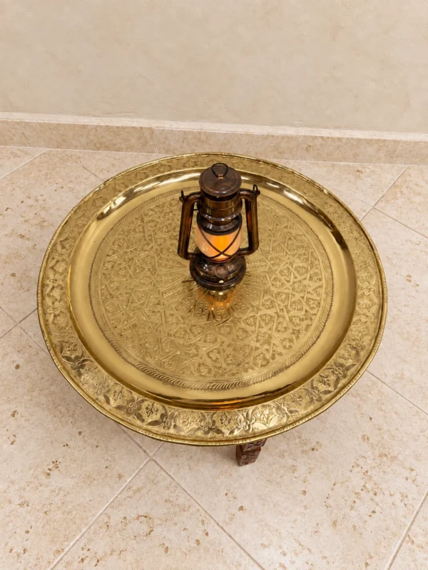 Round hand-engraved brass tray seen from above, with a geometric star pattern in the centre and a floral border on the rim.