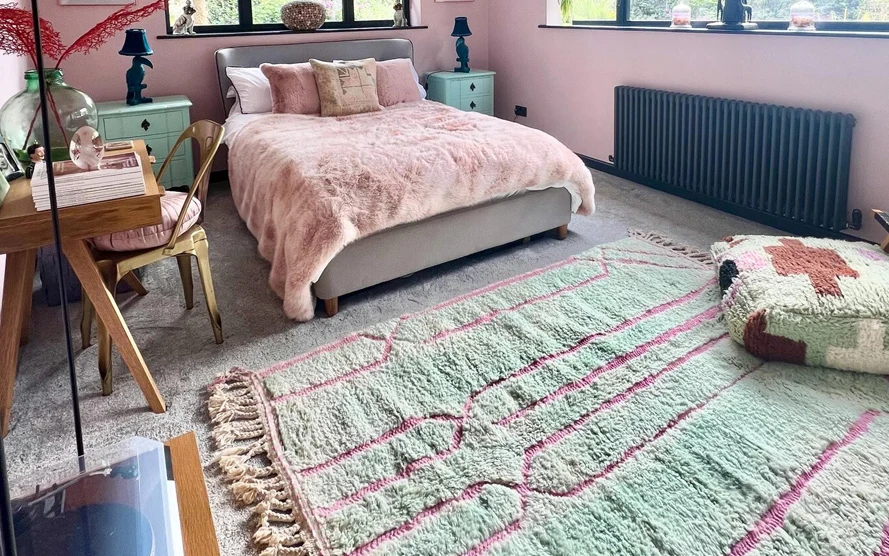 Green and pink custom-made Moroccan rug with fringe at the foot of a bed in a bedroom