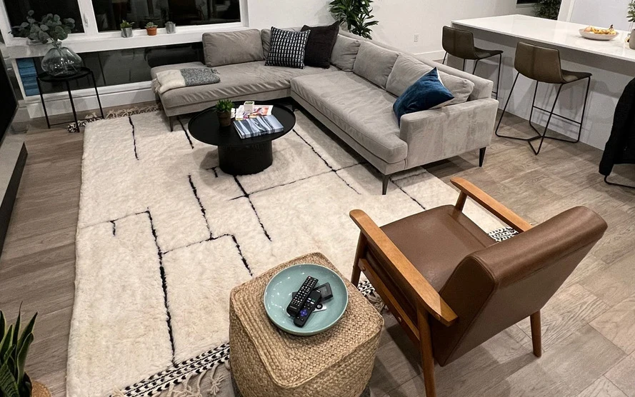 Ivory custom-made Moroccan rug with dark line pattern under a sectional sofa, coffee table and armchair in a living room