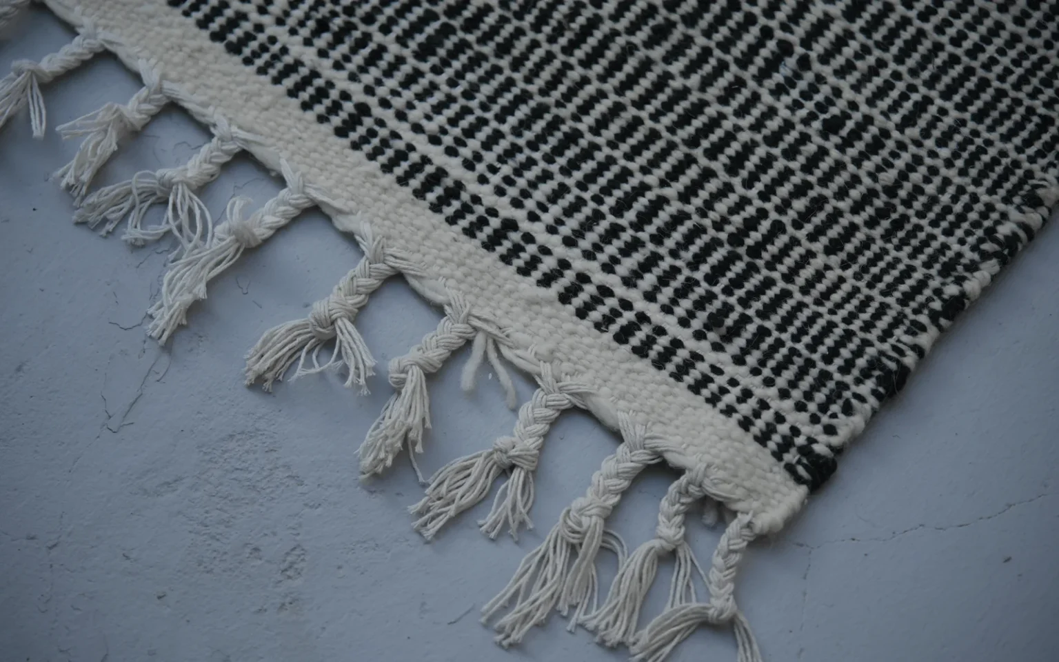 Close-up of the handwoven black and ivory wool weave and hand-finished fringe of a Zanafi rug