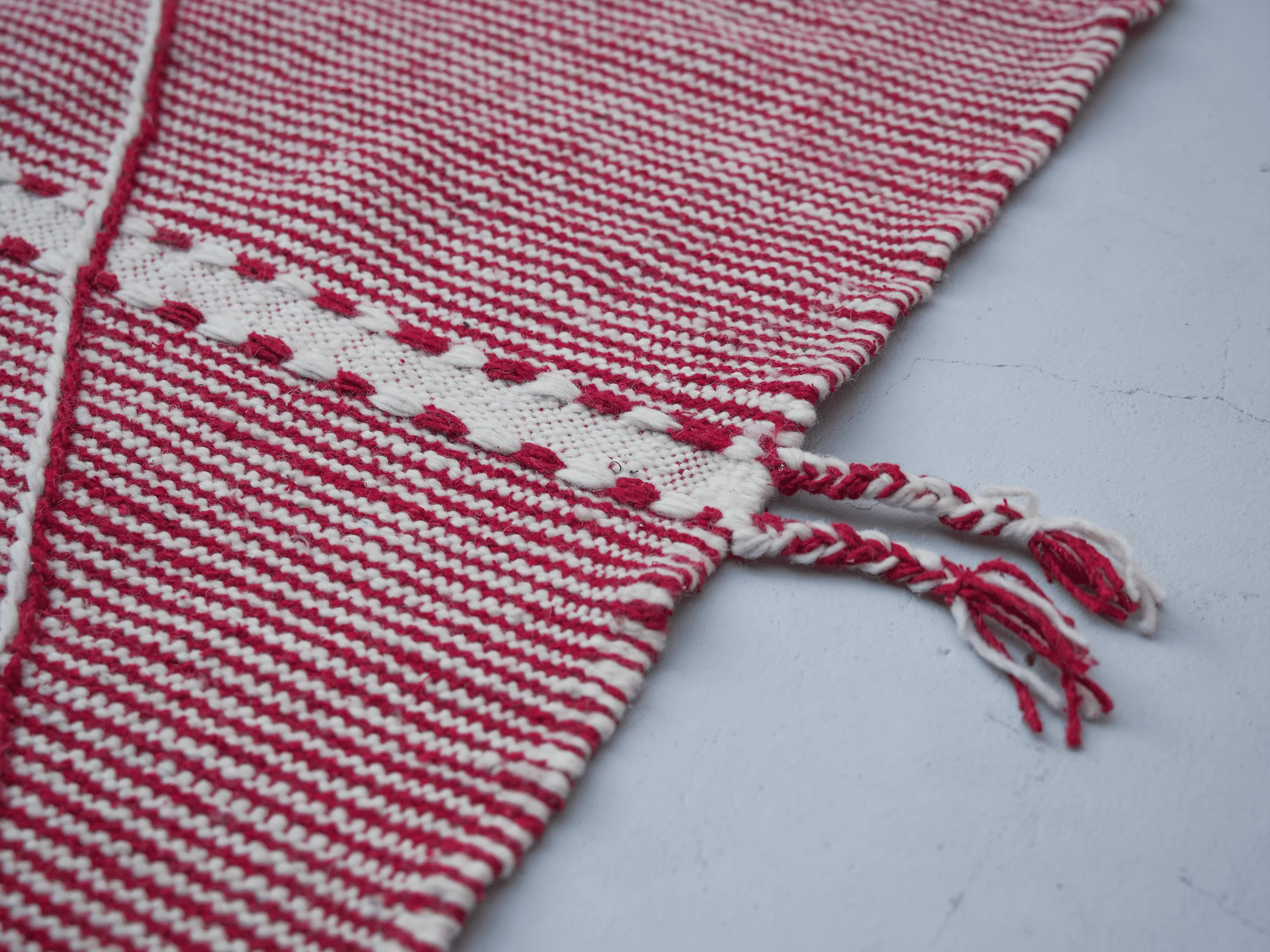 Detail of a Zanafi wool rug showing textured red and ivory weaving and twisted two-tone side tassels.