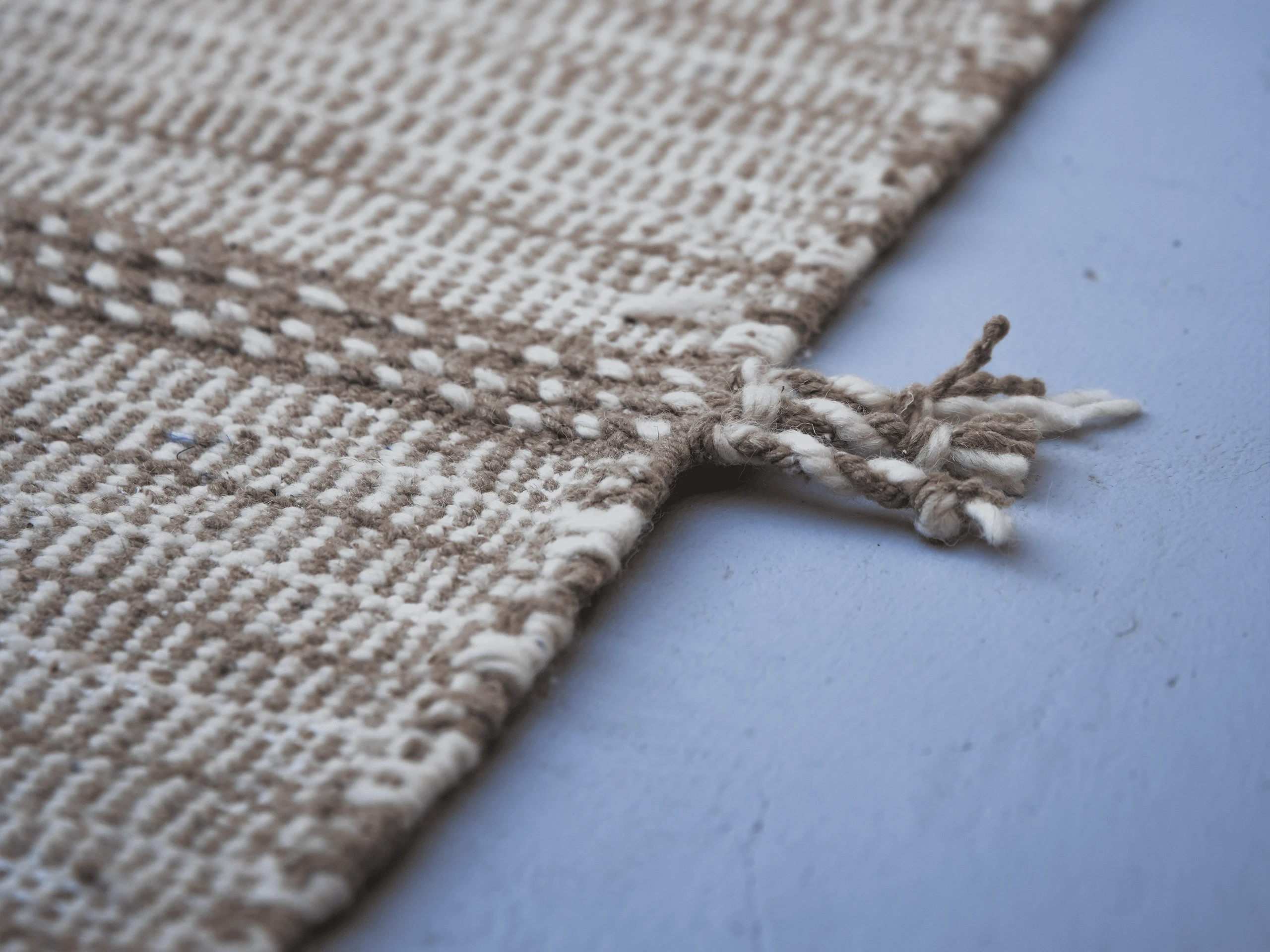 Detail of a small side tassel and woven band on a beige Zanafi wool runner.