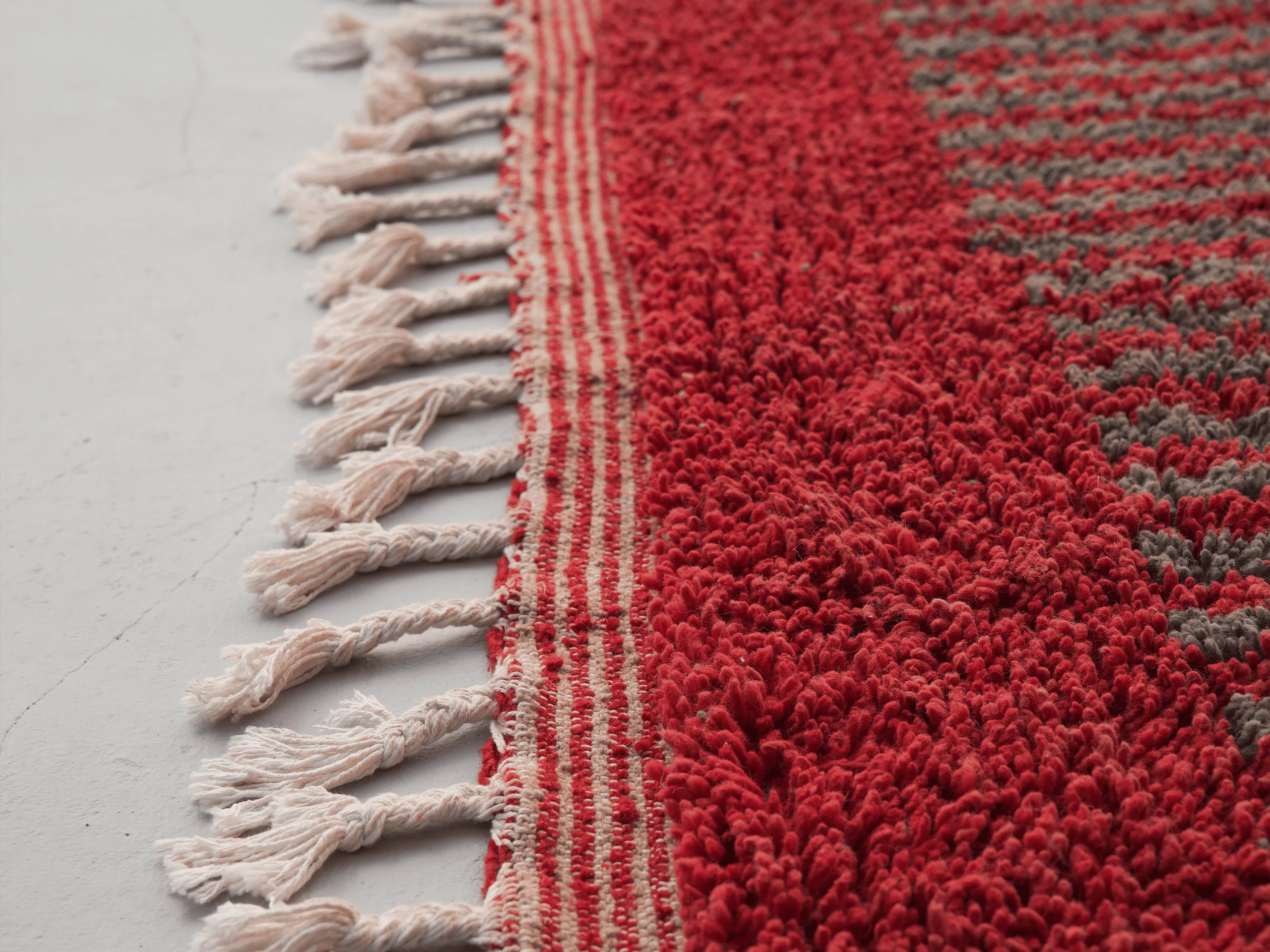 Detail of ivory tassels, the finely striped woven edge and red wool pile on a Boujaad-style rug.