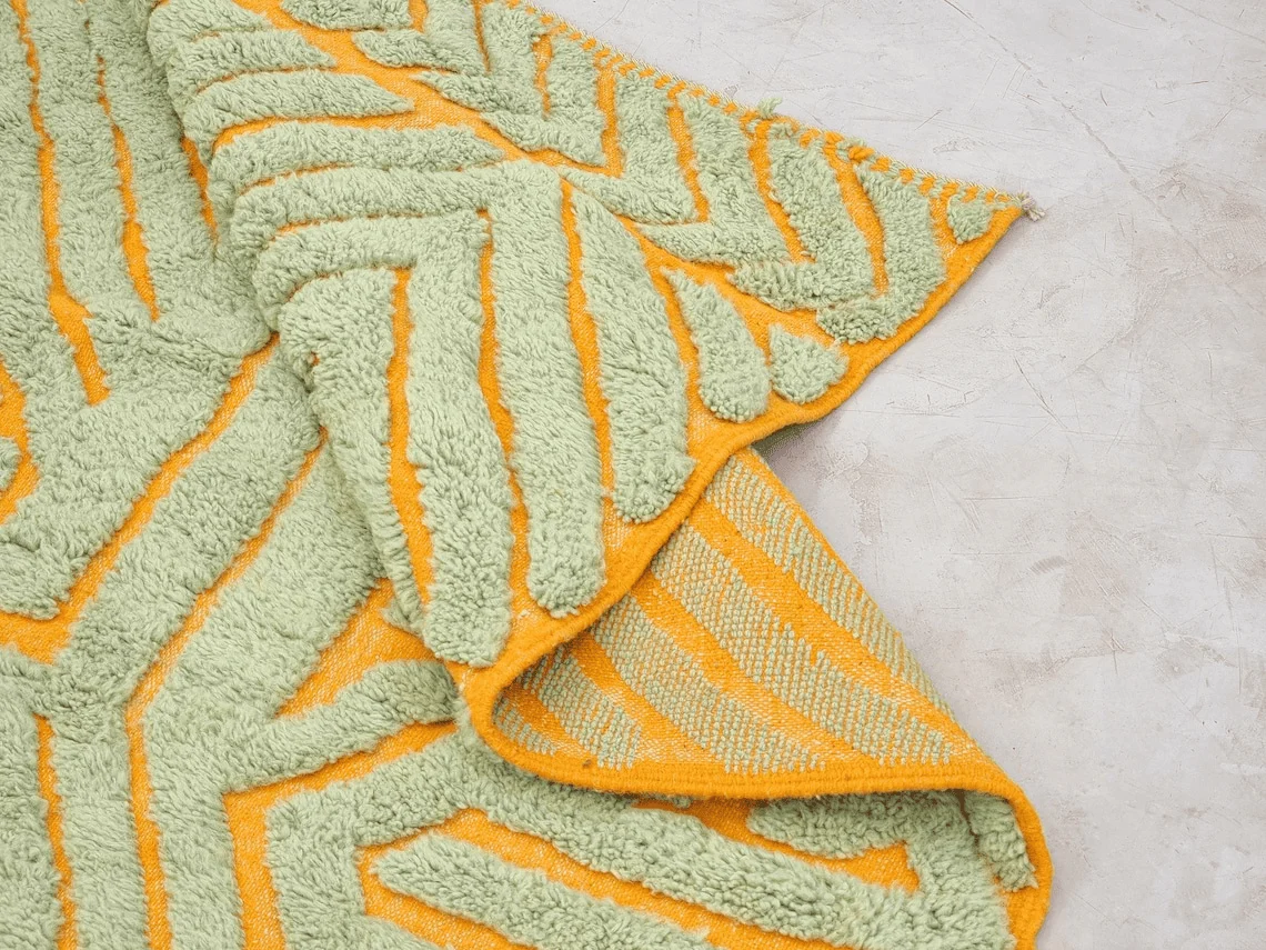 Folded corner showing raised sage green wool shapes, a lower golden orange woven base and the patterned reverse.