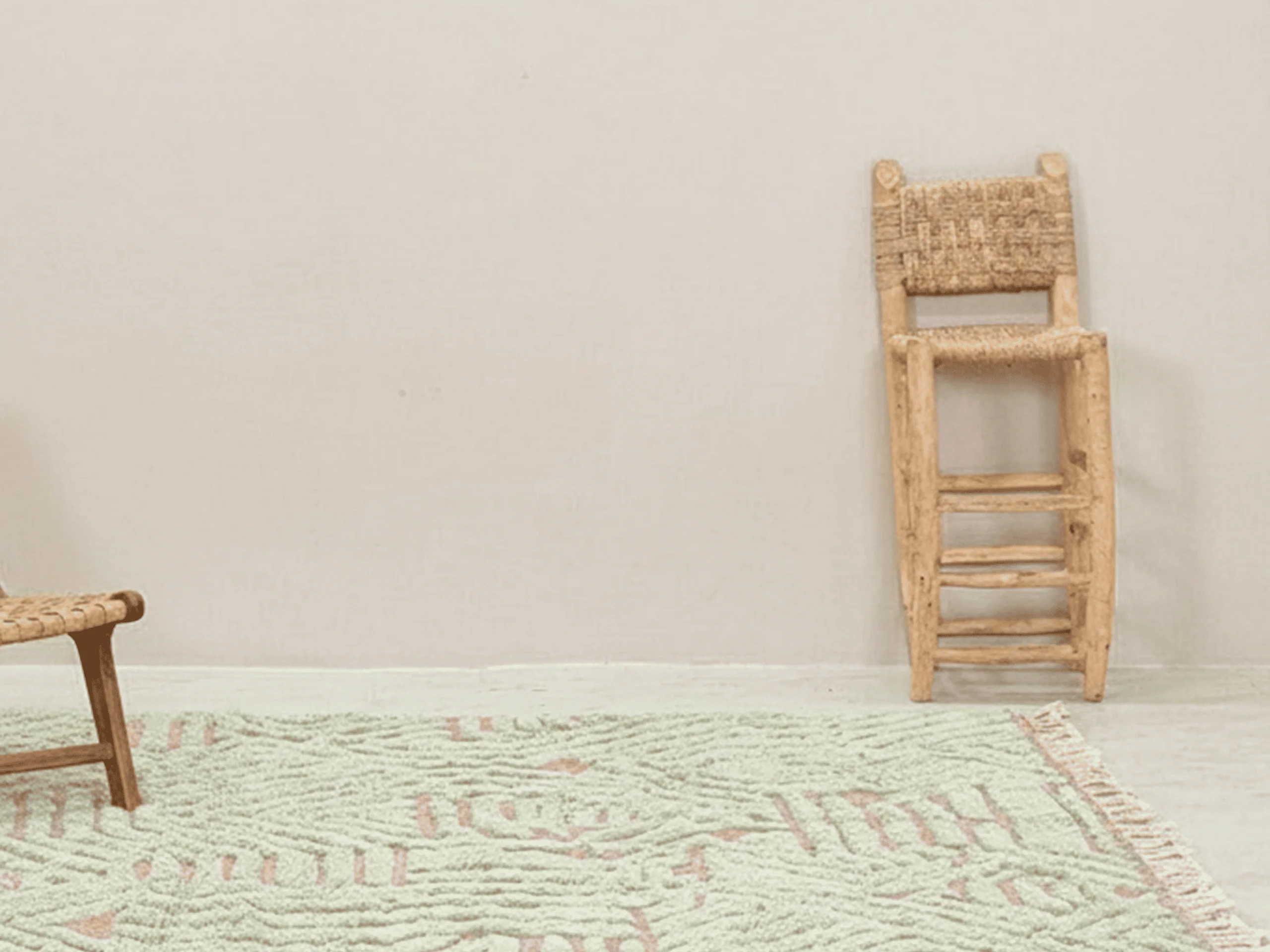 Pink and sage green textured wool rug on a light floor beside a tall woven stool.