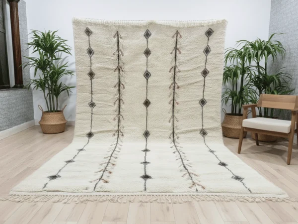 Ivory rug with diamond lines hung against a wall and spread onto a pale wood floor, with palms and a wooden armchair.