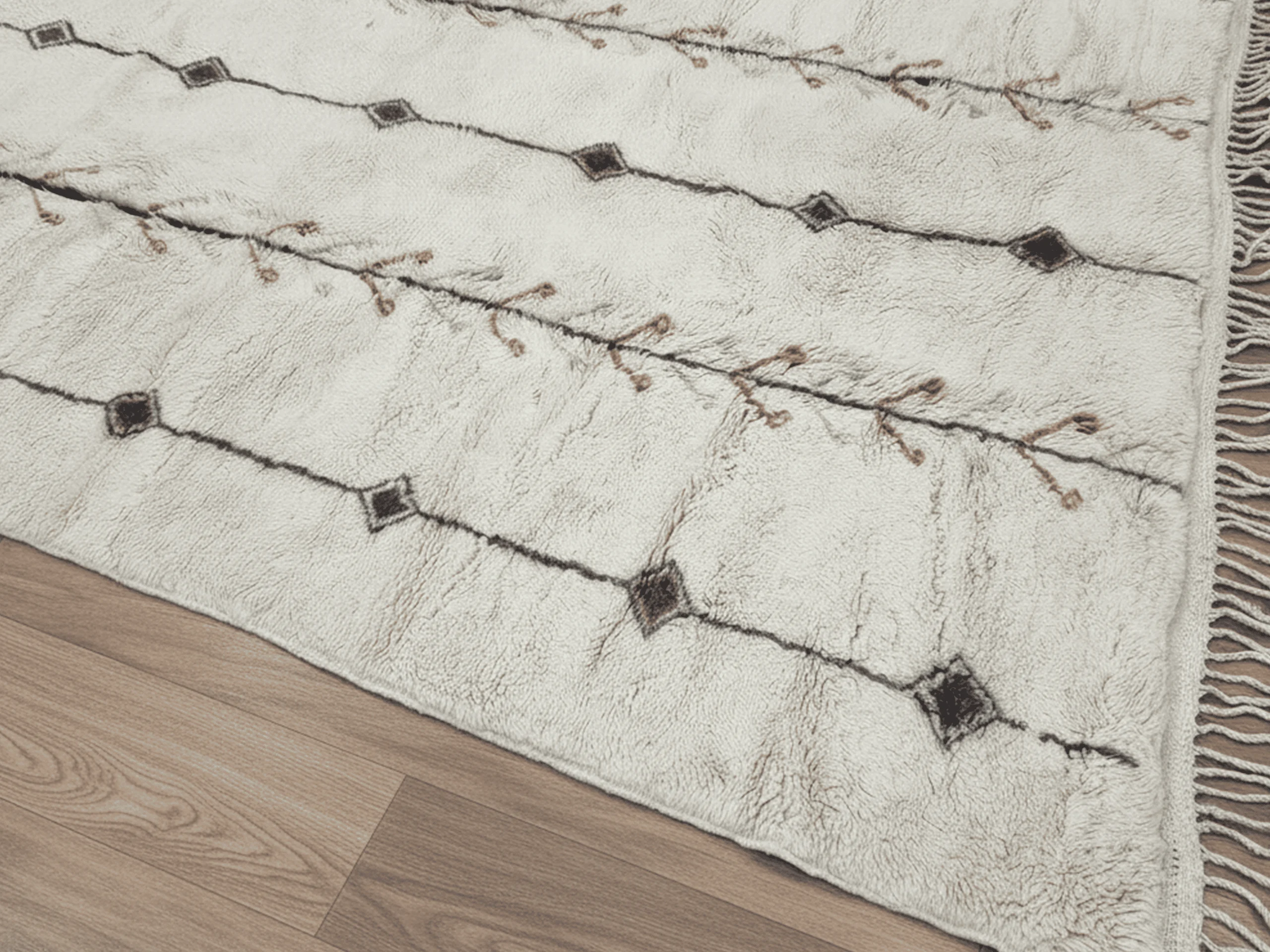 Close-up of charcoal diamonds and a rust-marked line across thick ivory pile, with fringe at the edge.