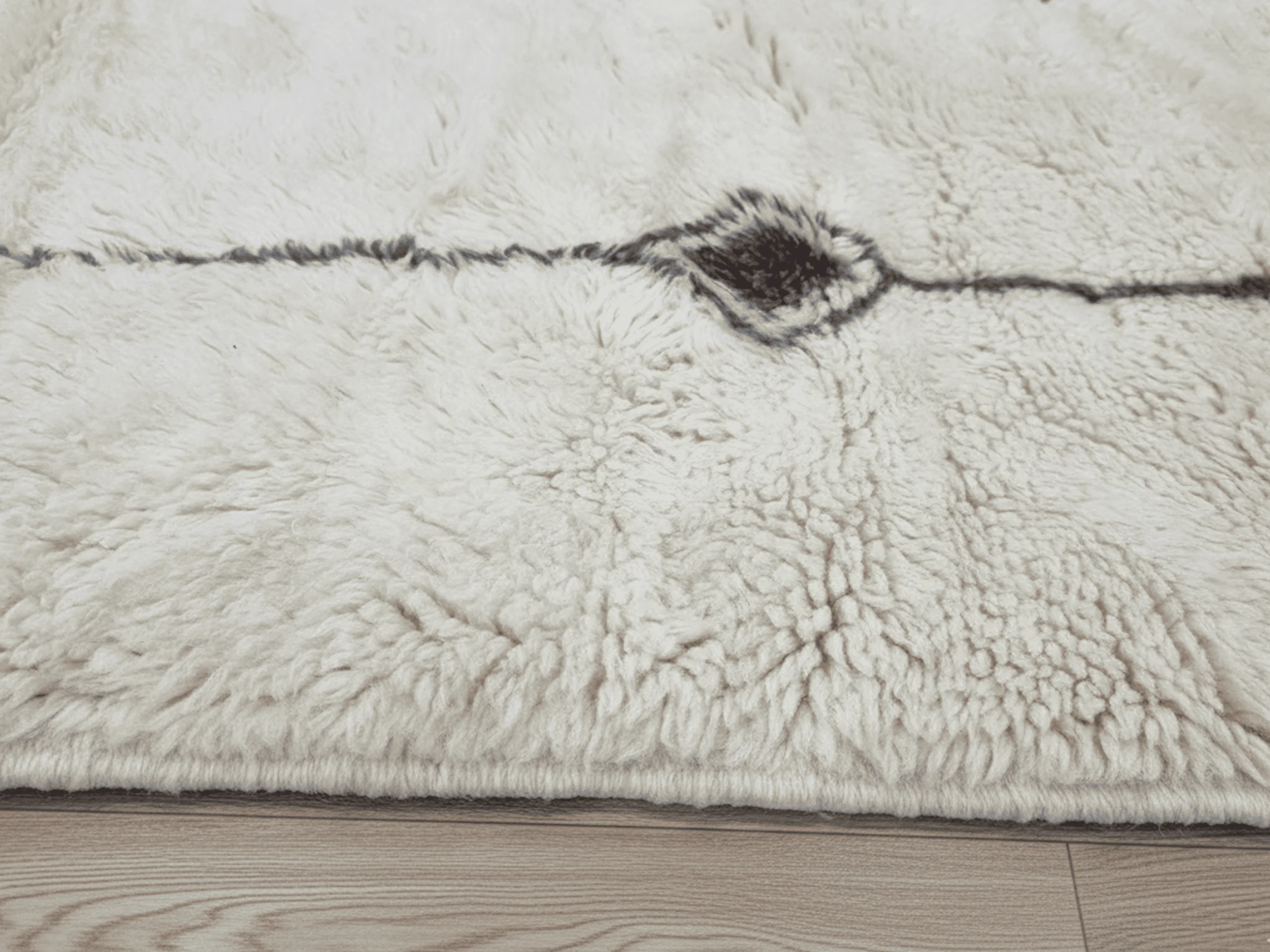 Macro view of thick ivory wool pile with a single charcoal diamond on a thin line.