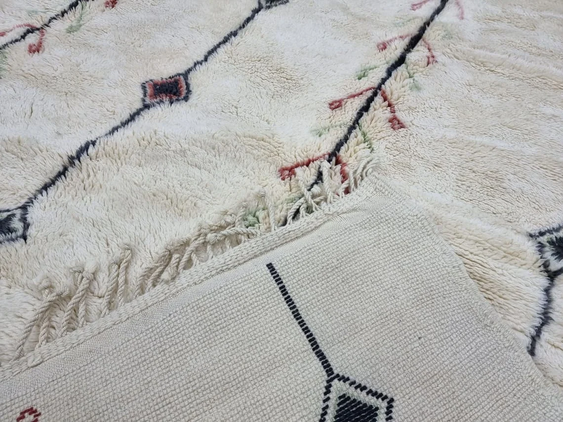 Folded corner showing the flat-woven reverse with a black diamond line, next to ivory pile with red and green marks.