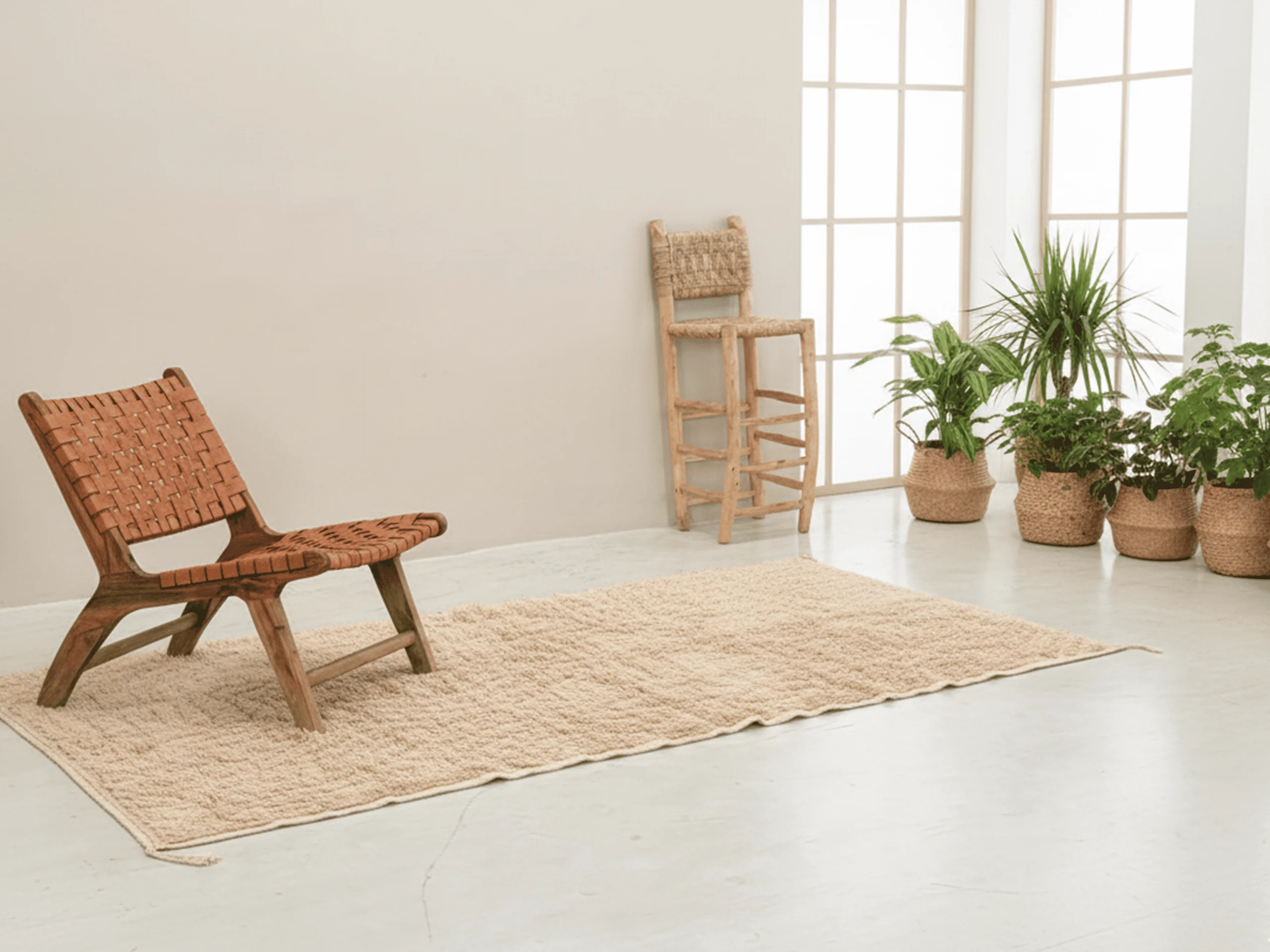 Woven leather lounge chair on the beige textured rug in a pale room with plants.