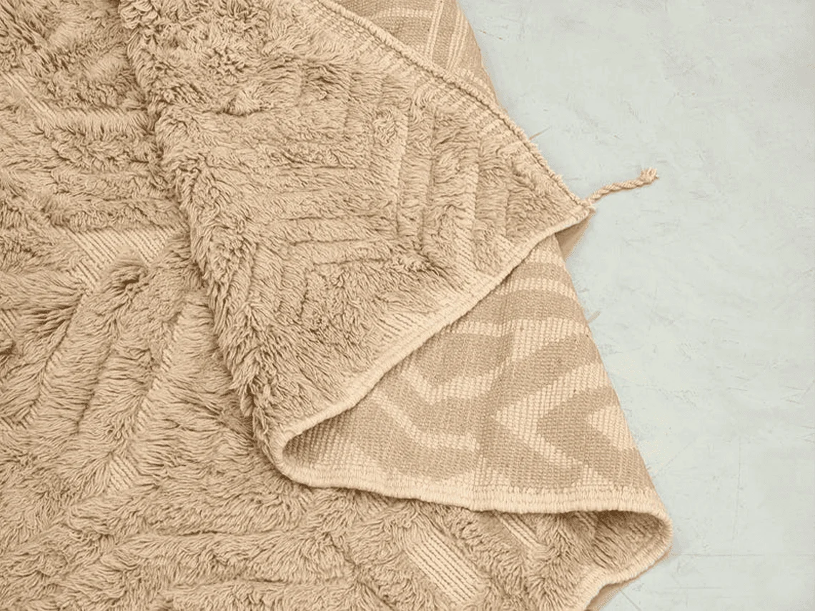 Folded section showing long beige pile on top and the flat-woven chevron reverse beneath.
