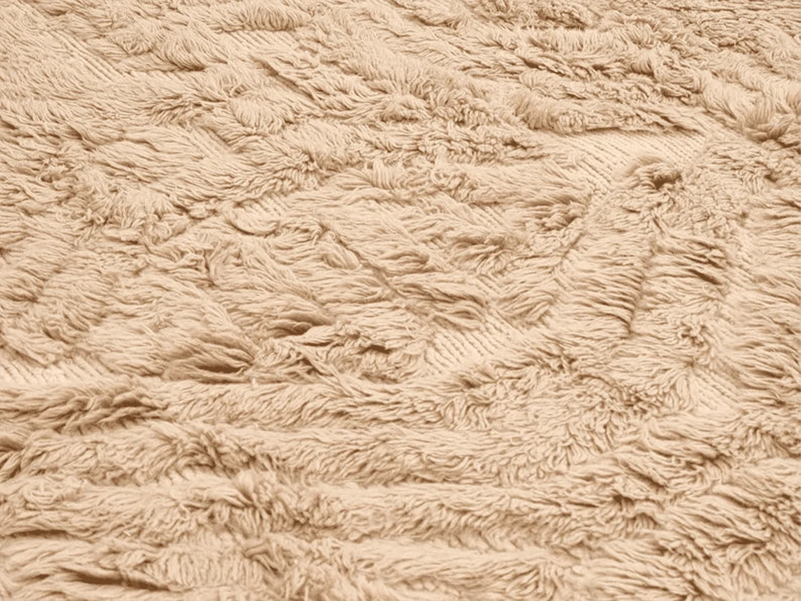Macro view of long beige wool pile with carved lines forming the relief pattern.