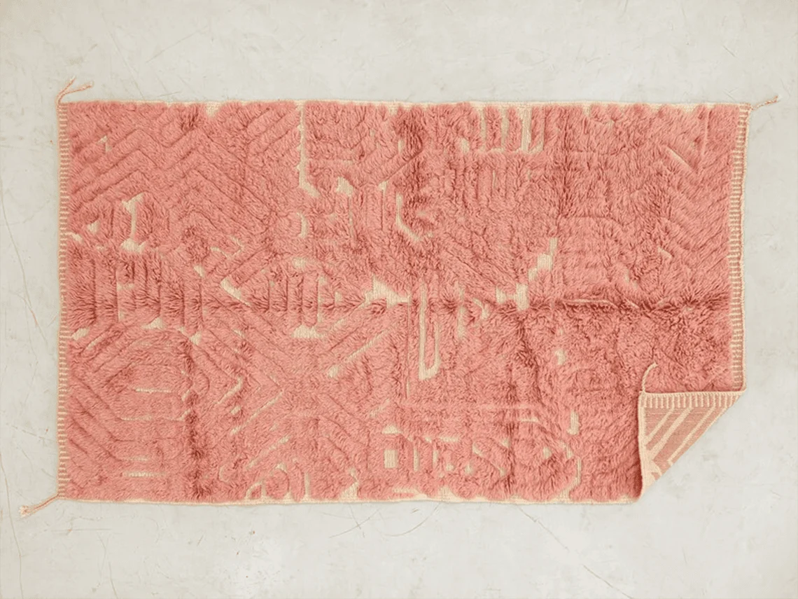 Top view of the coral pink rug with cream relief lines and a folded corner showing the striped reverse.