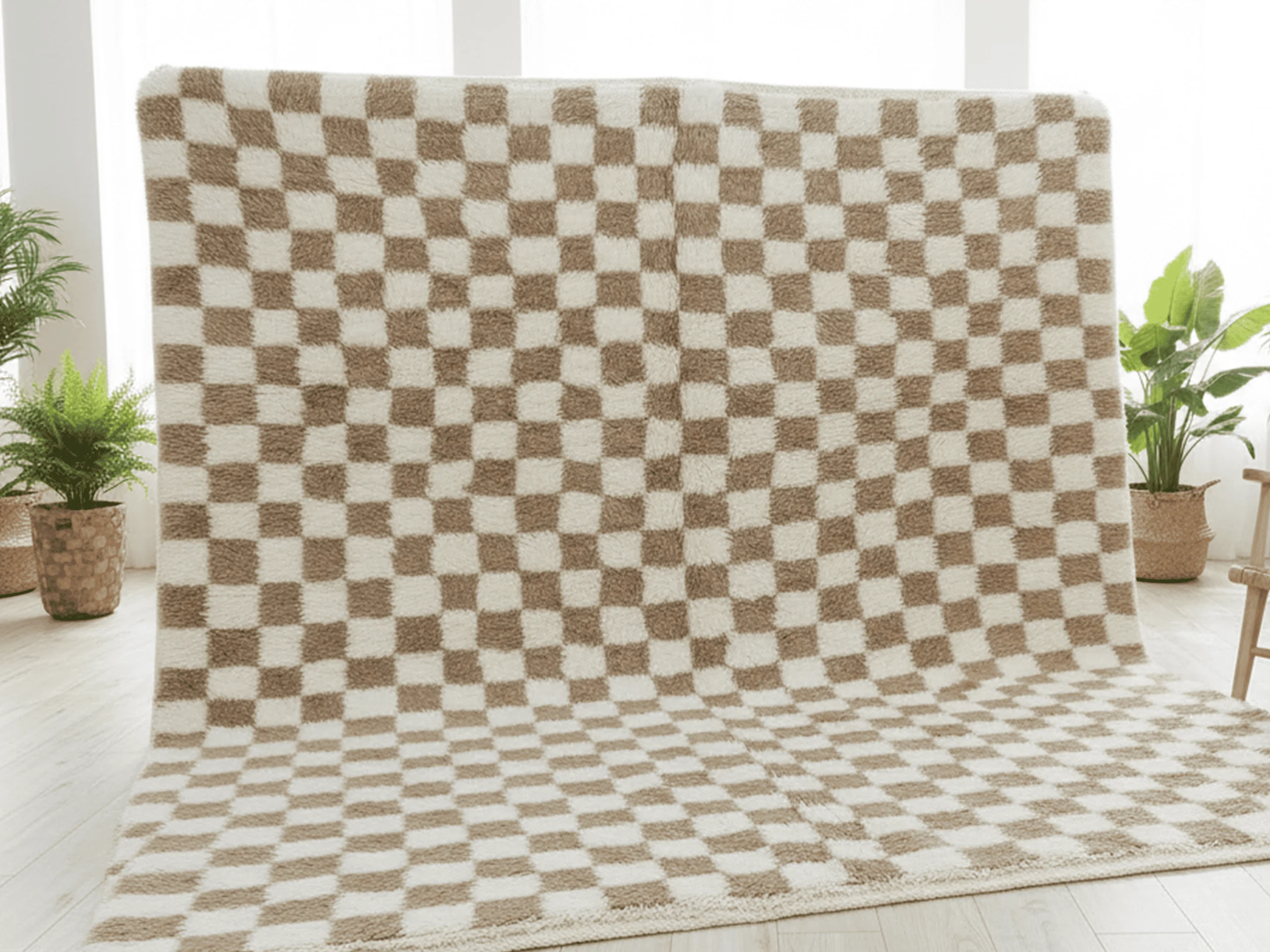 Checkerboard rug hung against a bright window wall and spread onto the floor, with plants on either side.