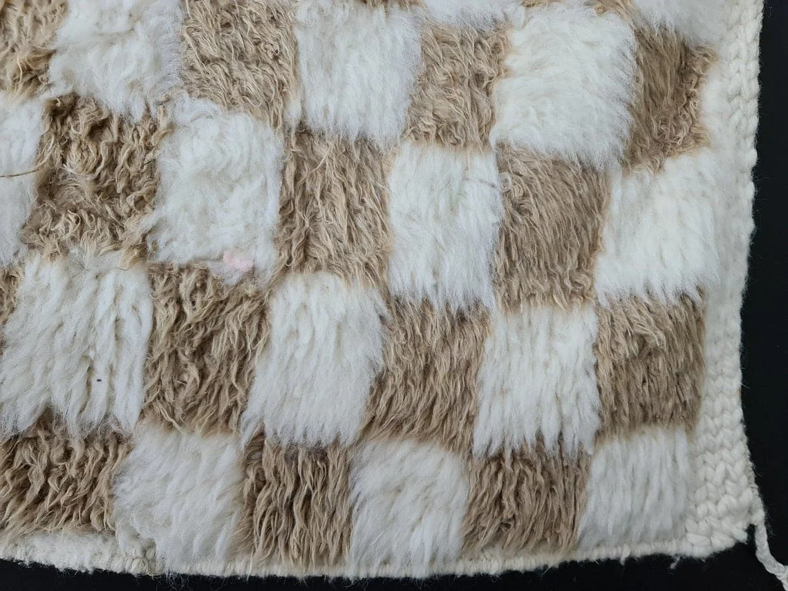 Close-up of thick beige and ivory wool squares with a braided ivory edge.