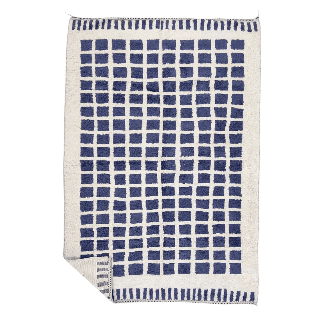 Ivory wool rug on a white background with a grid of indigo blue squares, dashed blue ends and a folded corner.