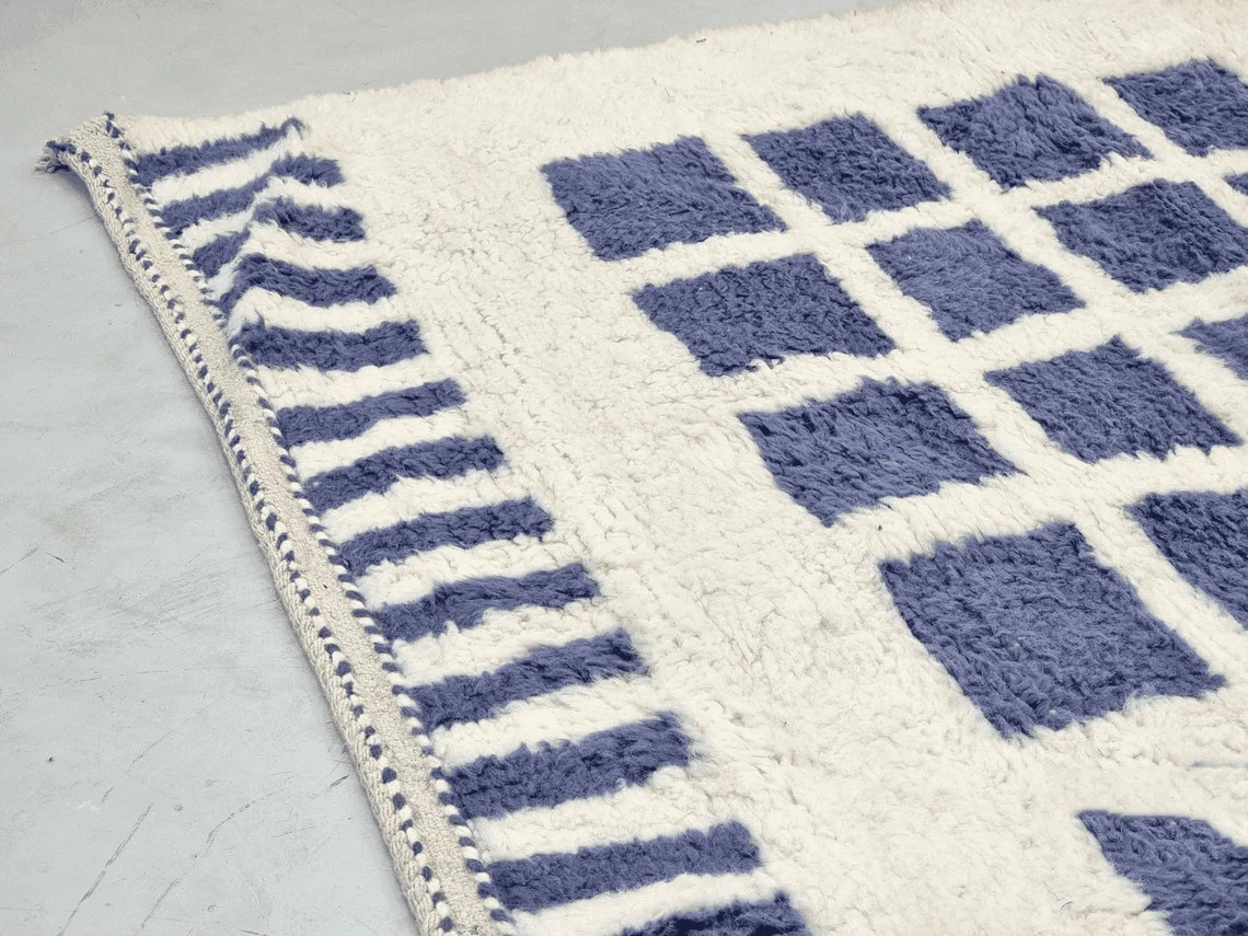 Close-up of the rug's edge with blue dashes, a braided trim and indigo squares in ivory pile.