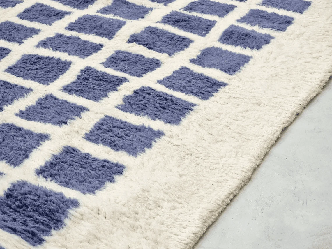 Close-up of indigo squares in shaggy ivory pile beside the wide ivory margin.