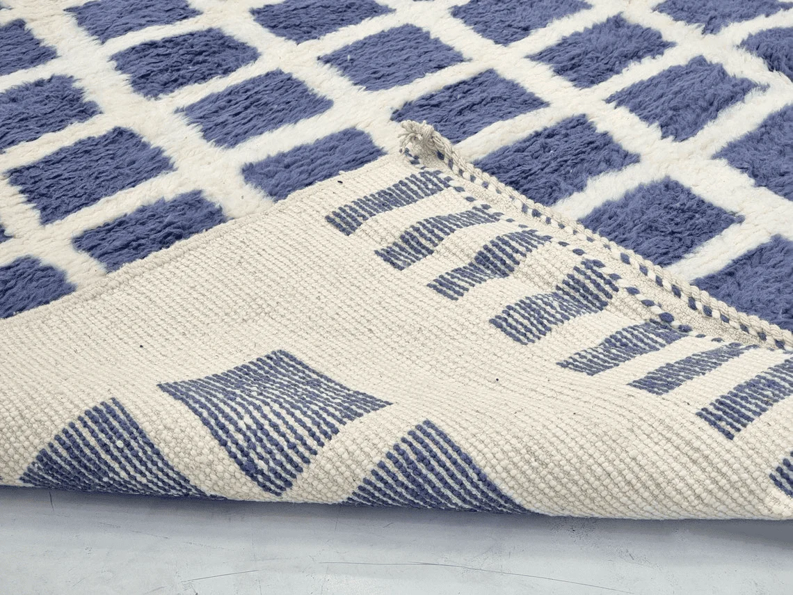 Folded corner showing the flat-woven reverse with ribbed blue blocks, on top of the shaggy front.