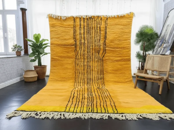 Yellow rug with black lines hung in a bright room and spread on a dark floor, with plants and a cane chair.