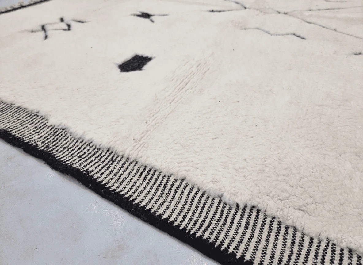 Close-up of the striped black and white border beside deep ivory pile with a small black symbol.