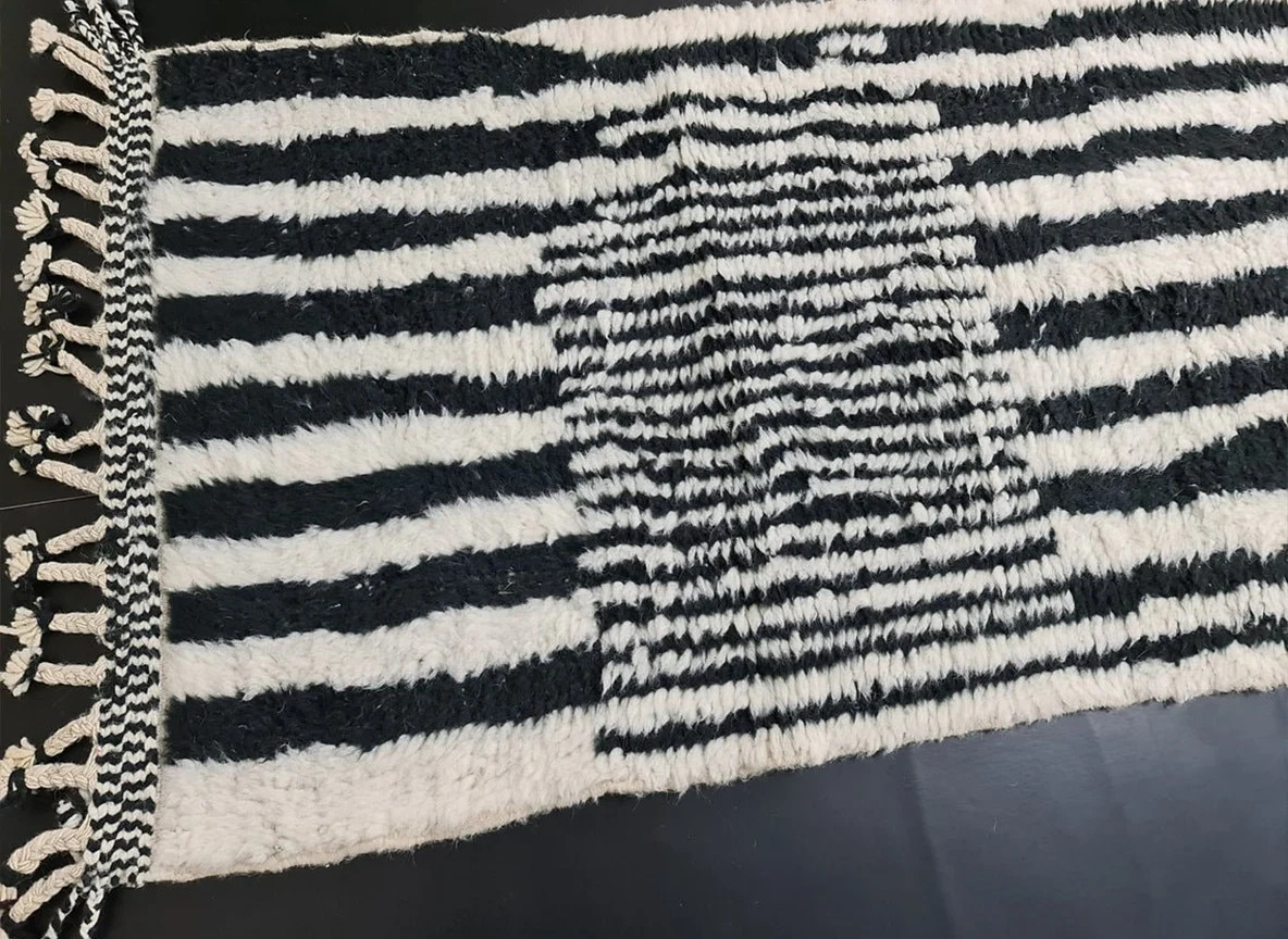 Close view of the runner's end showing black and ivory stripes, the fine-lined panel and a braided edge with fringe.