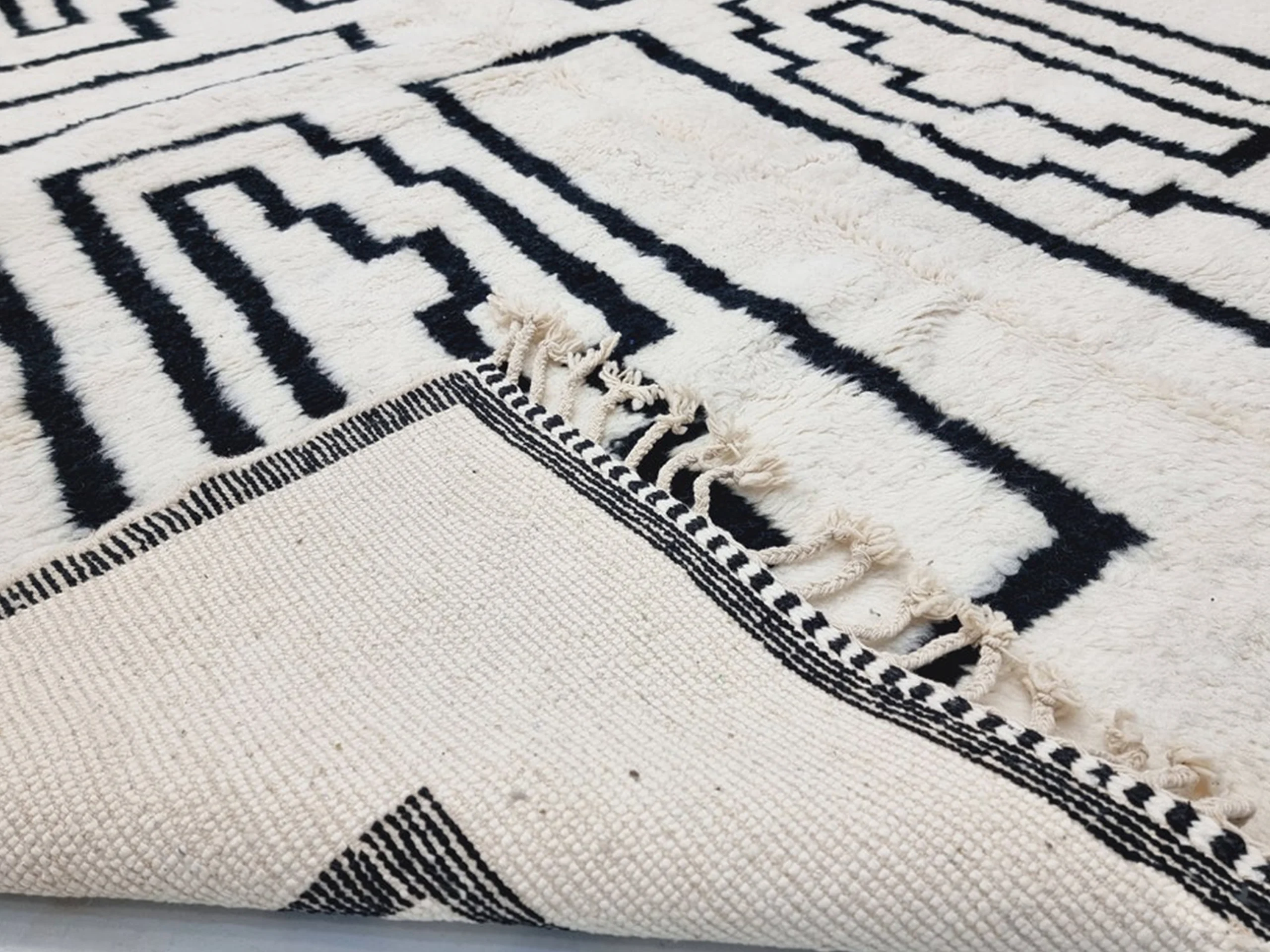 Folded corner showing the ribbed ivory reverse with black dashed lines, a striped edge and fringe.