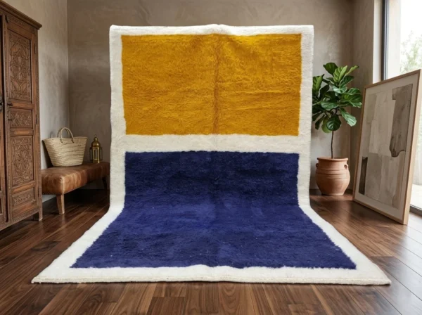 Navy and mustard color block rug hung against a wall and spread on a dark wood floor, with a carved cabinet and a plant.