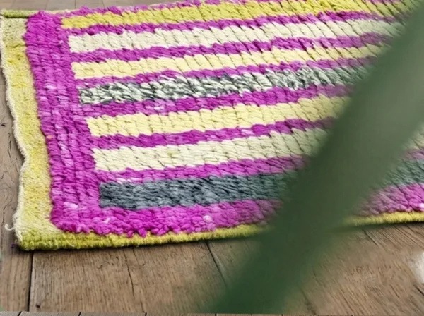 Corner close-up of magenta pile with cream, yellow and charcoal stripes and a mustard yellow edge.