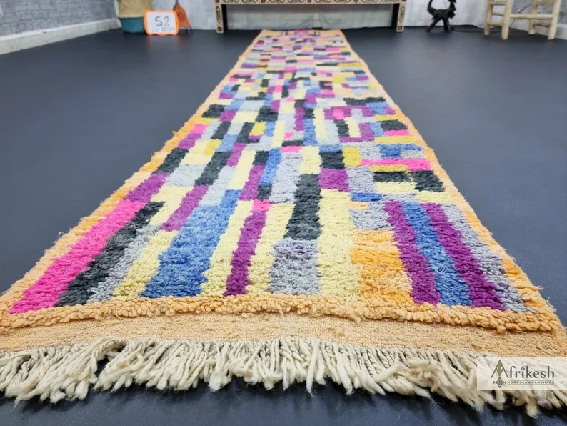 Lengthwise view of the multicolor patchwork runner on a dark floor, with an apricot edge and ivory fringe in front.