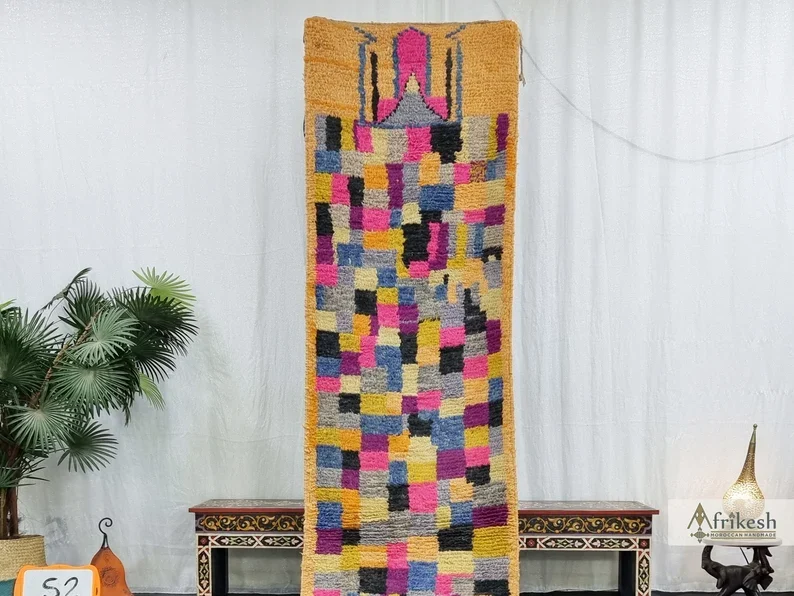 Upper part of the patchwork runner hung on a wall, showing the pink motif and blocks of pink, blue, gray and yellow.