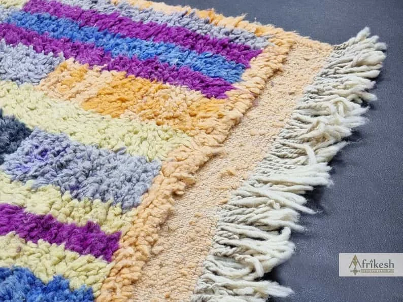 Corner close-up of shaggy blocks in purple, blue and yellow with an apricot border and ivory fringe.
