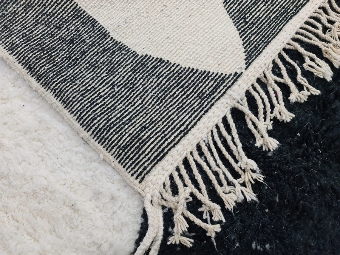 Folded corner showing the black and ivory striped flat-woven reverse with twisted fringe.