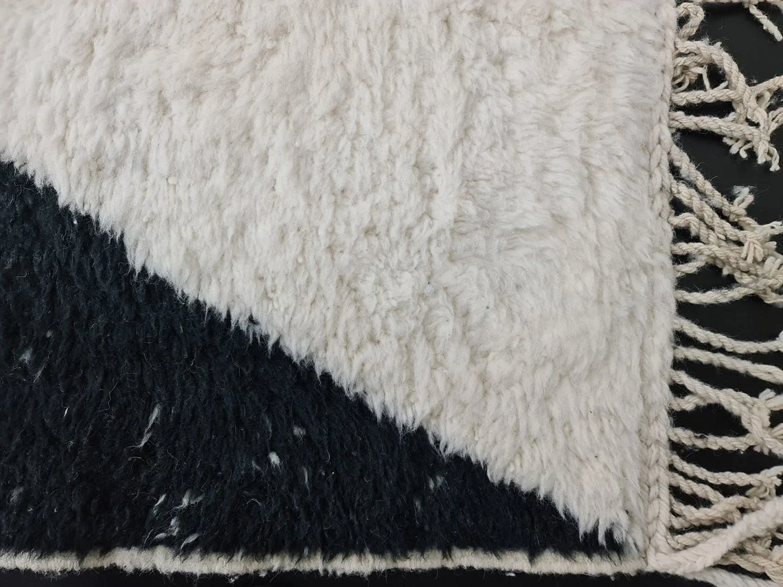 Corner close-up of deep ivory pile meeting black pile, with fringe along the side.