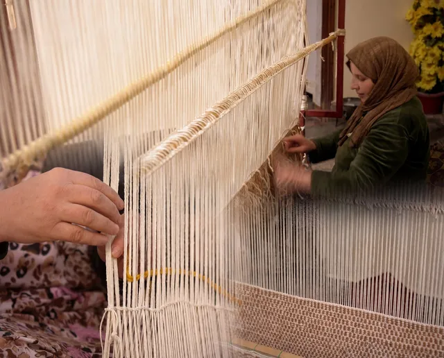 A weaver knotting wool at an upright loom.